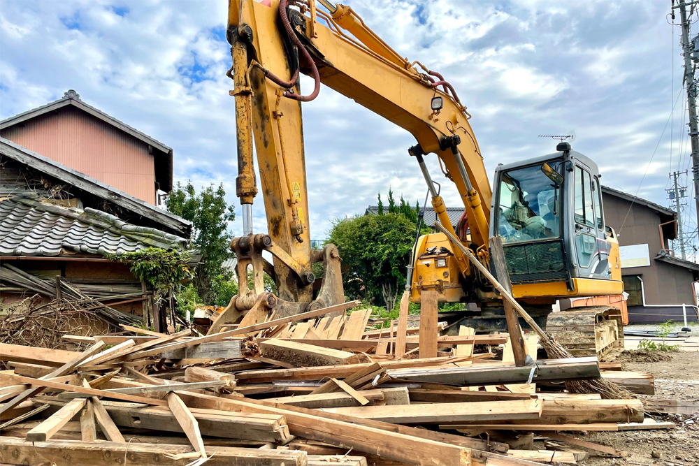 重機による木造家屋の解体作業。空き家解体に伴う残置物撤去の現場風景。